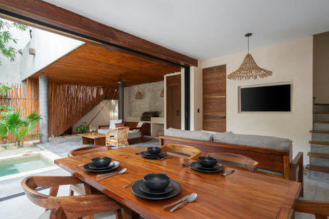Experience open-plan living with a dining space facing a vibrant tropical patio. Warm lighting, natural wood tones, and woven details make this area perfect for relaxation.