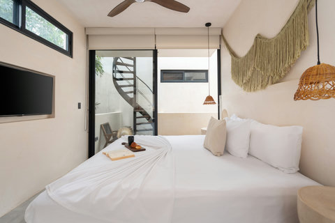 Elegant boho-style bedroom featuring a king-size bed, wall-mounted TV, and warm rattan lighting. The private balcony includes a spiral staircase leading to an exclusive rooftop terrace.