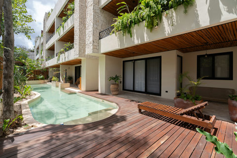 Stunning outdoor pool area with a unique curved design, wooden deck, and lush tropical surroundings. Ideal for relaxing, sunbathing, and enjoying a peaceful resort-style atmosphere.