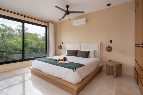 Elegant bedroom with a king-size bed, warm tones, and large windows showcasing lush greenery. A bright and peaceful retreat designed for ultimate comfort and relaxation.