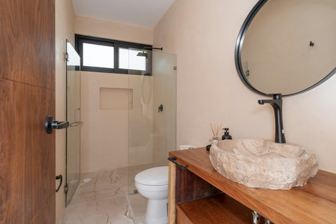 Modern bathroom with a glass-enclosed shower, natural stone sink, and warm wood vanity. Bright and functional, designed for a refreshing and comfortable experience.