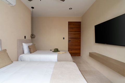 Modern twin bedroom with clean lines, soft neutral tones, and a wall-mounted TV. A comfortable and functional space designed for a relaxing stay.