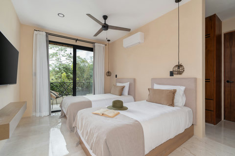 Bright bedroom with two comfortable beds, soft neutral tones, and a private balcony with lush jungle views. A relaxing and airy space perfect for restful stays.