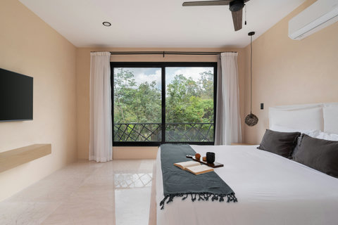 Bright bedroom with a king-size bed, floor-to-ceiling windows, and lush jungle views. A serene and airy space designed for rest, comfort, and natural connection.