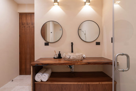 Elegant bathroom with a double vanity, natural stone sink, and warm wood finishes. Thoughtfully designed with soft lighting for a refined and relaxing atmosphere.