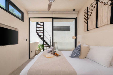 Relax in a bright boho-style bedroom featuring artisan décor, a plush bed, and direct access to a private terrace with a stylish spiral staircase and outdoor seating.