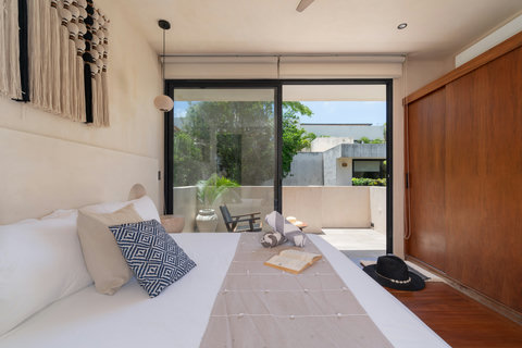 Relax in a bright and stylish bedroom featuring warm wood accents, boho décor, and direct access to a private balcony. A peaceful retreat filled with natural light and comfort.