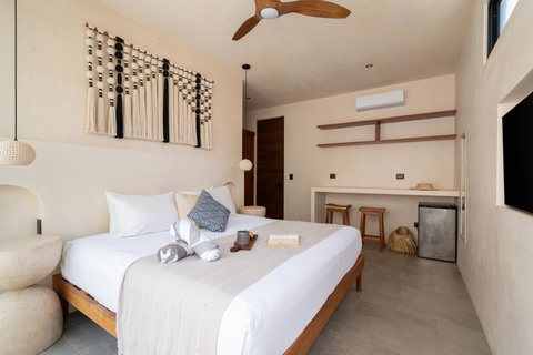 Relax in a spacious boho-inspired bedroom featuring artisan wall décor, warm neutral tones, and a plush bed designed for comfort and restful tropical escapes.
