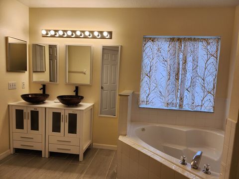 Master room en-suite bath with dual vanities, a bath tub, shower, iron, ironing board, and a large walk-in closet.