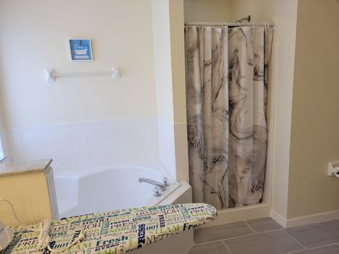 Master room en-suite bath with dual vanities, a bath tub, shower, iron, ironing board, and a large walk-in closet.