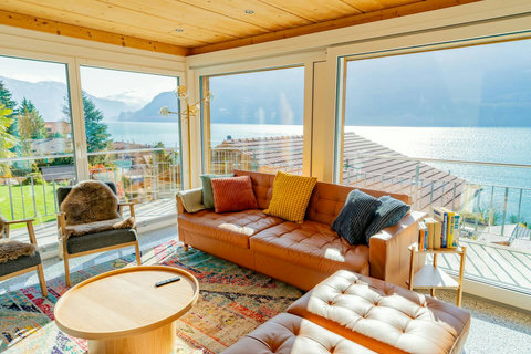 Where Design Meets Nature! ☀️ This bright, open-plan living room frames your private, floor-to-ceiling view of Lake Brienz and the stunning Swiss Alps. Experience luxury comfort on leather seating while enjoying the Swiss Dream Living scenery.