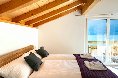 Attic Suite with Workspace. Enjoy privacy in this top-floor bedroom featuring a dedicated workspace (desk), attached washroom, and direct balcony access. The exposed wood beams and light-filled space define a premium Swiss Dream Living stay.