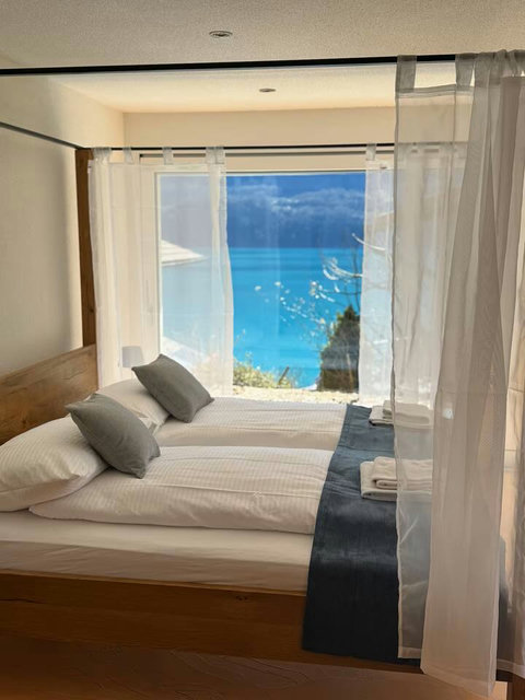 Unbeatable Lake View. This comfortable four-poster bedroom offers immediate, captivating views of the turquoise lake. High-quality bedding ensures a restful Swiss Dream Living stay.