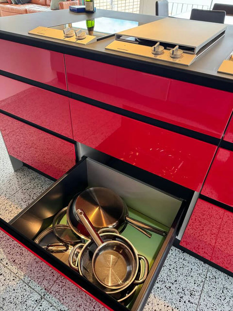 Gourmet Tools at Hand. High-gloss red cabinetry opens to reveal full, organized kitchen equipment. Every detail is ready for your culinary adventures at Swiss Dream Living.