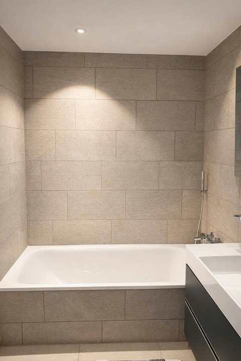 Modern bathroom with a full-size bathtub, neutral stone tiles, and a clean, minimalist design.