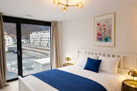 A peaceful second bedroom featuring a double bed, warm lighting, and large windows with views of the town and surrounding landscape.