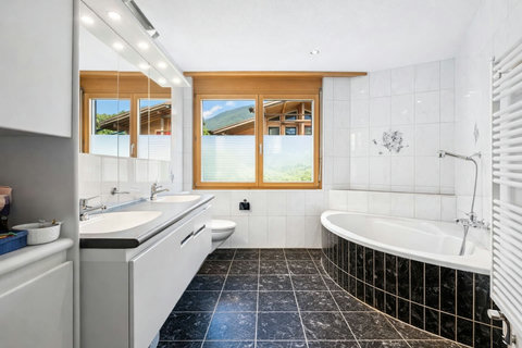 Spacious ground-floor bathroom with bathtub, double vanity and bright mountain views for a relaxing alpine stay.