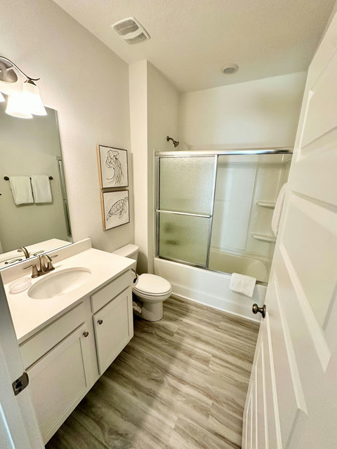 Clean bathroom with tub-shower and coastal art