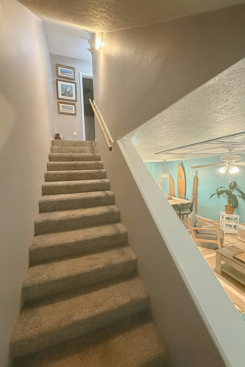 Stairway overlooking teal living room and surfboard wall