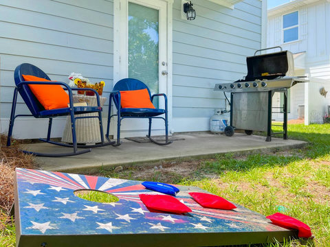 Backyard patio with grill, rockers, and cornhole