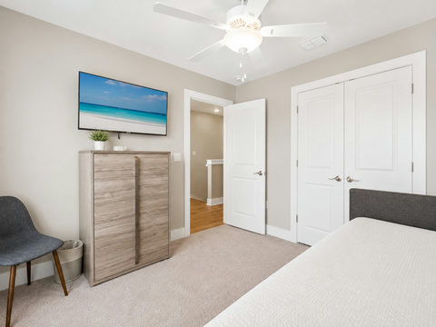 Bedroom – Serene bedroom with a coastal-mural TV over a wood dresser and an accent chair.