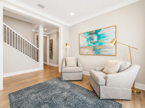 Living Room – Cozy sitting nook with accent chairs, a vibrant blue abstract painting, and a view of the staircase.