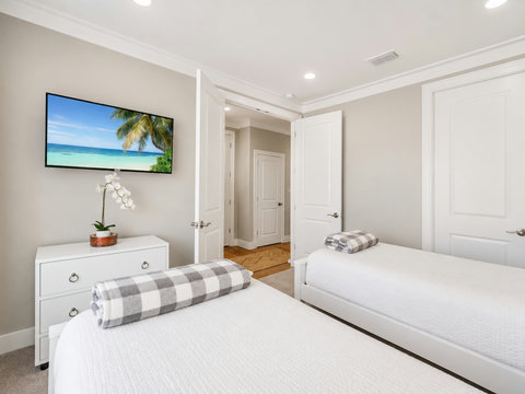 Bedroom – Versatile guest room with a mounted beach-scene TV, dresser, and cozy bedding.