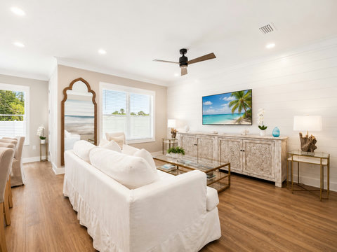 Living Room – Comfortable sitting area with a slipcovered sofa, media console with mounted TV, and an elegant arched floor mirror.