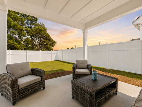 Outdoor Living – Covered patio with cushioned lounge seating overlooking a private fenced backyard at sunset.