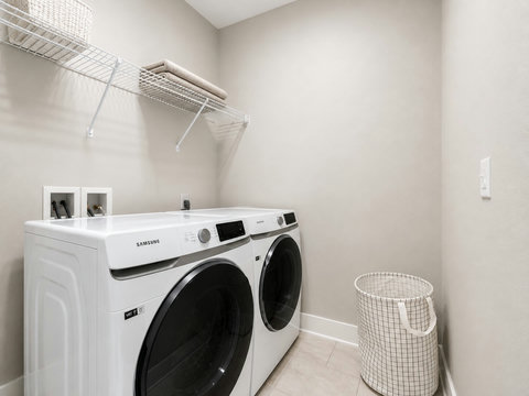 Laundry Room – Full-size front-loading washer and dryer with drying rack and storage.
