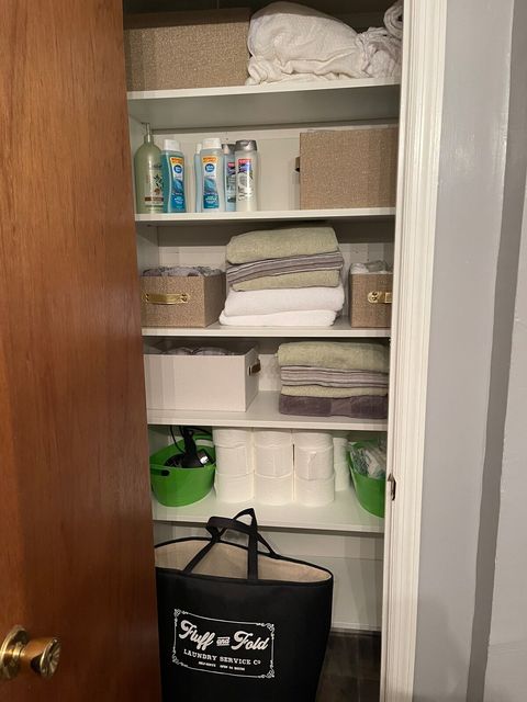 Master bath linen closet with king sheet sets, towels, body wash, shampoo, conditioner, toilet paper, shower liner, hair dryer and laundry basket.  King sheet sets are in the gold bins.
