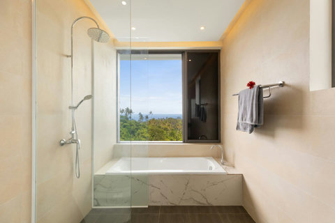 Luxurious bathroom with soaking tub, rainfall shower and tropical garden views through picture windows