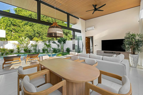 Open-plan living and dining with wooden table, comfortable sofa and stunning pool-garden views - perfect for gatherings