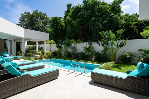 Tropical villa exterior with vibrant blue pool, comfortable sun loungers and lush mature gardens in Bophut