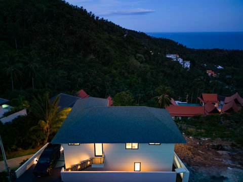 Aerial view of villa at dusk with jungle hillside surroundings and ocean backdrop - luxury retreat