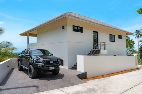 Bright daytime villa exterior with parking area - modern hillside architecture and convenient access