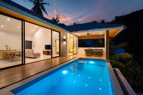 Illuminated pool terrace at twilight with glass doors opening to living area - luxury villa ambiance