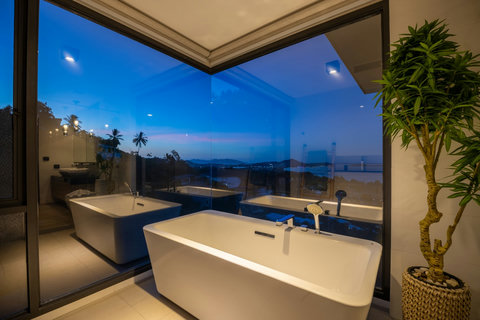 Bathroom with freestanding tub and floor-to-ceiling sea views at dusk at Villa Yoco, Koh Samui