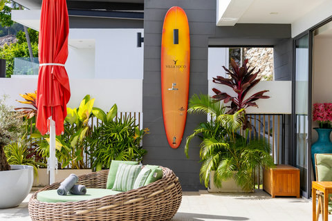 Villa entrance with covered rattan seating, surfboard and tropical planting at Villa Yoco, Koh Samui