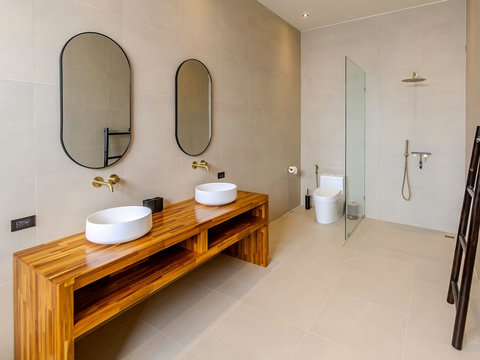 This bathroom feels like a private spa retreat. Double sinks and a spacious wooden vanity sit before a walk-in shower, with lush greenery visible beyond