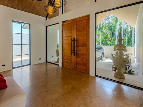 Step into a bright, airy foyer with soaring wooden beams and natural light streaming through large glass doors. The space feels welcoming and designed for easy movement