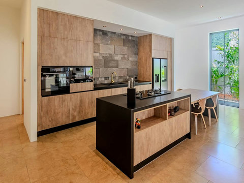 Cook in this bright modern kitchen where wood tones and clean lines meet natural light. Windows frame the green gardens beyond.