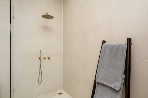 Start your day with a luxurious rainfall shower in this serene ensuite. Gold fixtures and clean cream tiles create a spa-like calm