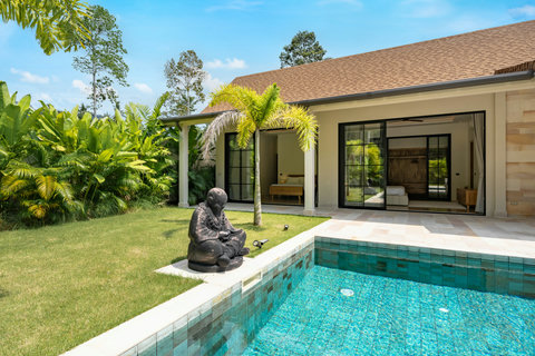 A peaceful stone figure sits among towering palms and vibrant plants, inviting quiet reflection in the garden sanctuary.
