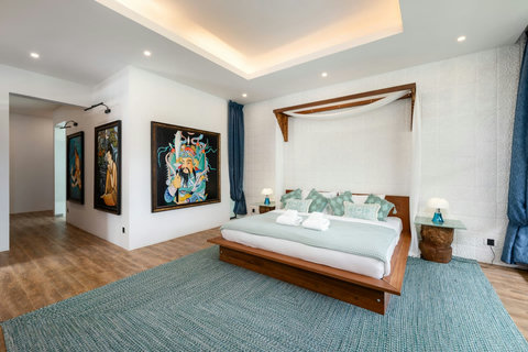 Spacious bedroom with vibrant artwork, plush teal carpet, and garden views