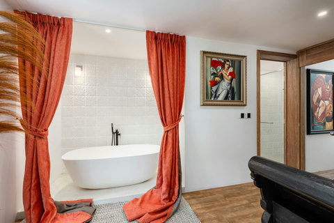 Elegant en-suite bathroom with freestanding soaking tub, rich wood accents, and artwork
