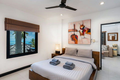 Bright modern bedroom opening to private balcony with palm tree and ocean views at Sunview Koh Samui