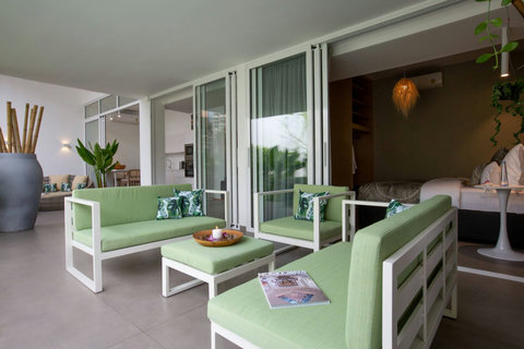Covered outdoor lounge with plush green sofas surrounded by tropical gardens at C Villa, Koh Samui