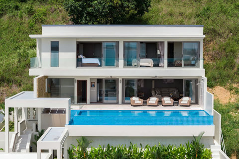Modern hillside villa with infinity pool overlooking the lush tropical landscape. Floor-to-ceiling glass doors for a seamless indoor-outdoor experience.