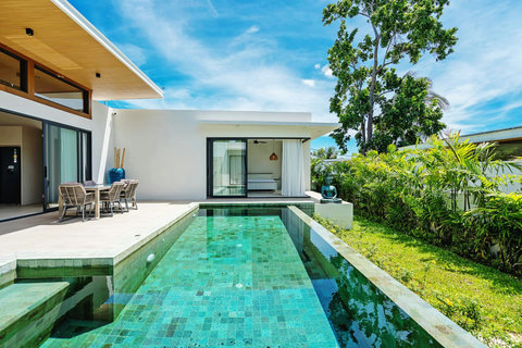 Daytime infinity pool with tiled sun deck, alfresco dining and lush tropical garden